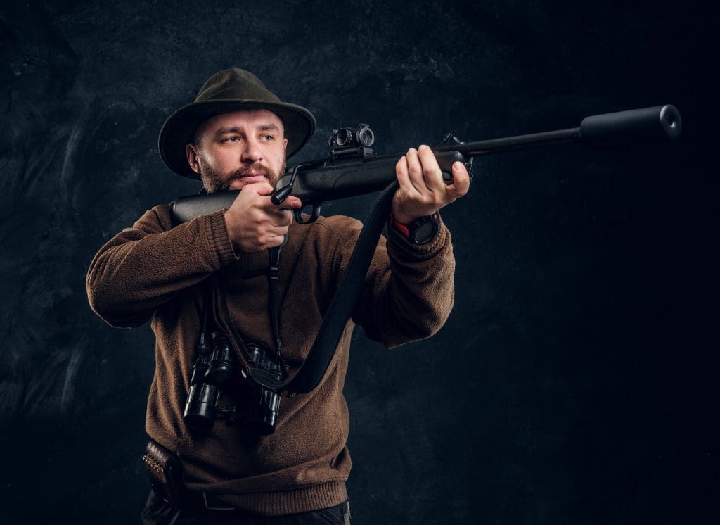 Portrait of a Bearded Hunter Holding a Rifle Studio Photo Against Dark Wall Background